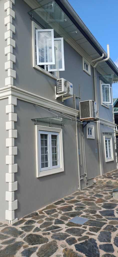 Completed new residential building exterior in Point Fortin, showing grey walls, white window mouldings and finished exterior surfaces.