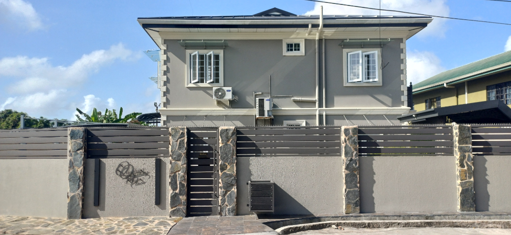 Wide view of the completed grey new residential building with white trim behind the front boundary wall.