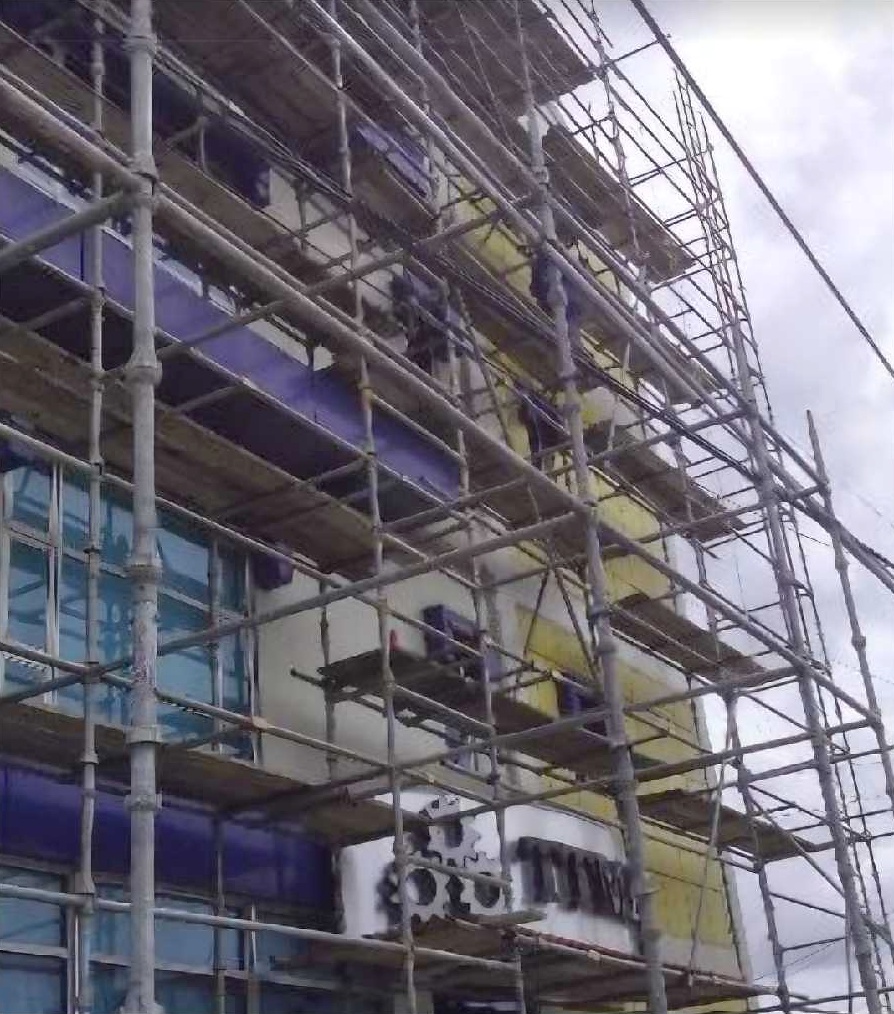 Multi-storey building facade surrounded by pipe scaffolding and work platforms.